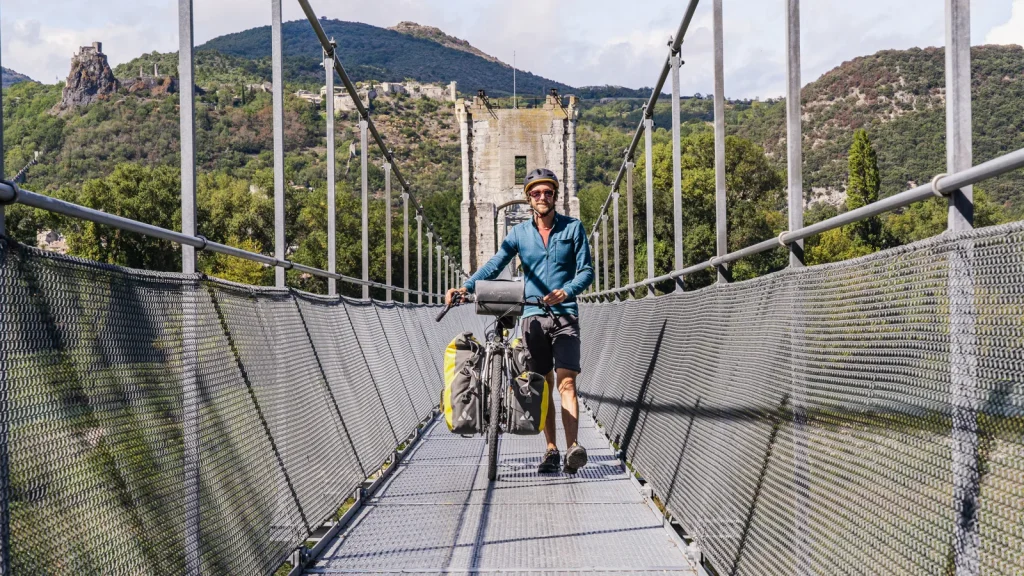 Man with his bike, on the himalayan footbridge in the village with outstanding character of Rochemaure, in winter. Roaming, he will join the ViaRhôna